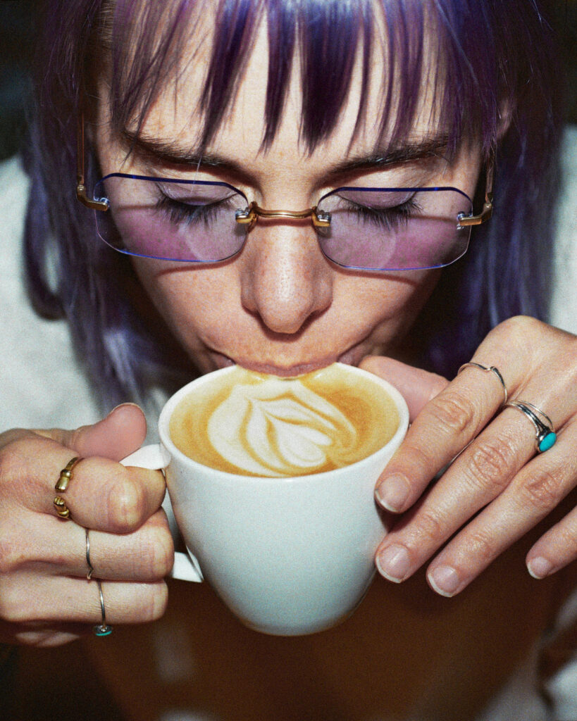 Frau mit einer getönten Brille nippt an ihrem Kaffee