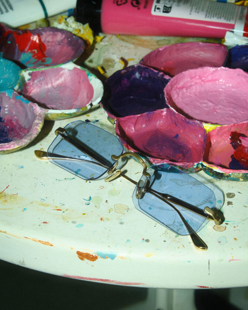 Blau getönte Brille liegt inmitten von Farbnäpfen in einem Atelier